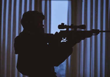 Pencerenin önünde kurban nişan maço silüeti. Avcı, asker silah çekimden önce nişan ile. Tetikçi kavramı. Adam silah, tüfek karanlık iç arka planda tanınmaz