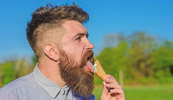 Conceito dos dentes doces. Homem de barba comprida lambe gelado. Homem com barba e bigode no rosto estrito come sorvete, fundo azul do céu, desfocado. Homem barbudo com cone de sorvete — Fotografia de Stock