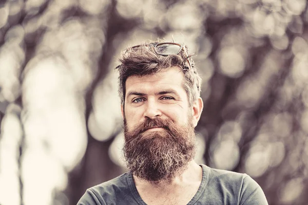 Hombre barbudo haciendo caras graciosas, frunciendo el ceño y levantando la ceja. Primer plano retrato de hombre guapo con barba larga al aire libre, divertido y activo concepto de ocio — Foto de Stock