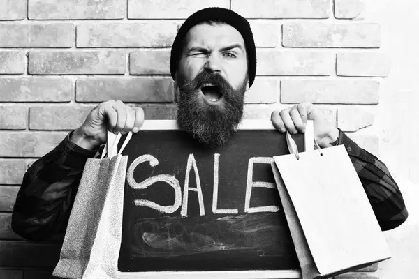 Hipster barbudo sosteniendo paquetes de compras y tablero con inscripción Venta —  Fotos de Stock