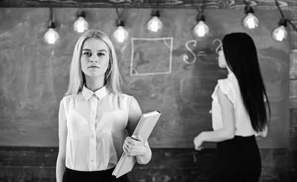 Estudiante, profesor de ropa formal en el aula. Mujeres atractivas preparándose para la lección. Chica se ve confiado, mientras que la señora escribiendo en el fondo de pizarra, desenfocado. Concepto de estudiantes y aprendices — Foto de Stock