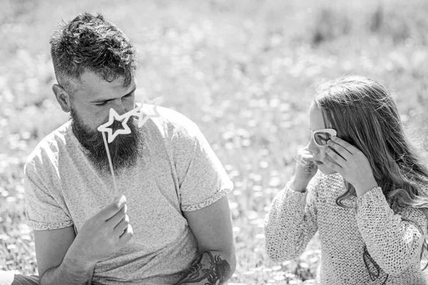 O pai e a filha sentam-se na relva no campo, fundo verde. Conceito de negociação. Família passar o lazer ao ar livre. Criança e pai posando com óculos atributo cabine de fotos ao falar — Fotografia de Stock