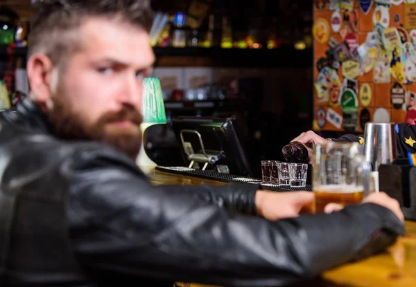 Brutal hipster bearded man sit at bar counter drink beer. Friday evening. Bar is relaxing place to have drink and relax. Man with beard spend leisure in dark bar. Hipster relaxing at bar with beer