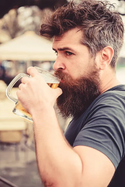Mannen med skägg och mustasch innehar glas med öl medan du kopplar av på kaféterrassen. Kille med resten med kall fatöl. Hipster på lugna ansikte dricka öl utomhus. Fatöl koncept — Stockfoto