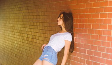 Kızı tuğla duvar arka plan poz rahat. Kadın duvara yalın verandada bekle. Birini bekliyor. Kız çekici esmer yeraltı geçidi veya metro takılmak rahatlatıcı. Metro kültür