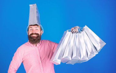 Sakallı adam aptal bakmak ve üzerinde mavi arka plan izole kocaman bir gülümseme ile. Erkek Alışverişkoliğin gümüş yetkin çantaları taşırken trendy sakallı. Mağaza, reklam kavramı teşvik satış salonu-assistand