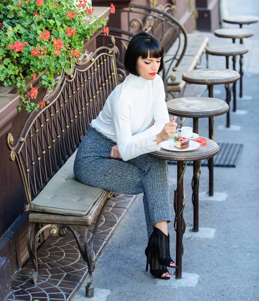 Woman attractive brunette eat gourmet cake cafe terrace background. Gastronomical enjoyment. Girl relax cafe with cake dessert. Pleasant time and relaxation. Gourmet concept. Delicious gourmet cake