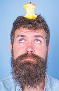 Canlı hedef kavramı. Adam yakışıklı hipster uzun sakal neredeyse kafasına elma güdük hedef olarak yem. Kilo kaybı gol. Hipster sürpriz yüz baş mavi arka plan üzerinde elma güdük hedefle yakın