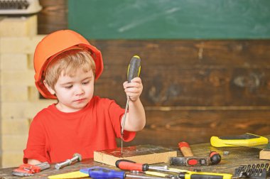 Tornavida ile çalışma meşgul bir çocuk. Turuncu kask vida ahşap blok içine bağlama içinde çocuk konsantre
