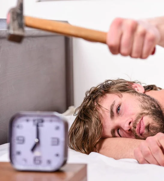 Un tipo tocando con un martillo sonando el despertador. Romper el régimen de disciplina. Un sonido molesto. Hombre barbudo molesto cara somnolienta yacía almohada cerca del despertador. Deja de sonar. Molesto despertador sonando —  Fotos de Stock