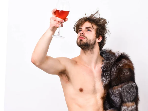 Estilo de vida y bienestar de lujo. Riqueza y concepto de lujo. Chico atractivo posando abrigo de piel en cuerpo desnudo. Sexy macho soñoliento tousled beber vino o alcohol aislado en blanco. Símbolo de lujo — Foto de Stock