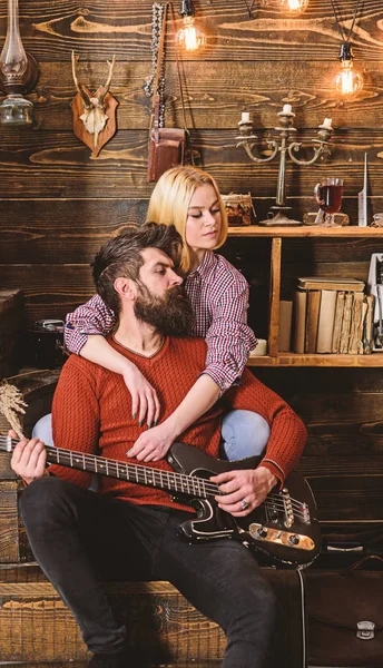 Señora y hombre con barba en caras de ensueño abrazos y toca la guitarra. Concepto romántico de noche. Pareja enamorada pasar una velada romántica en un ambiente cálido. Pareja en madera vintage interior disfrutar de la música de guitarra — Foto de Stock