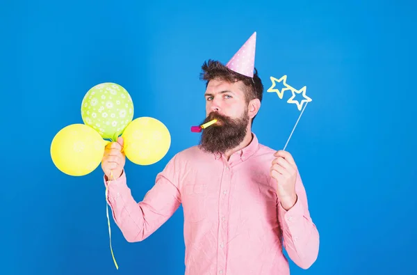 Skäggiga part underhållare barn Celebration, internationella barn dag koncept. Mannen med ljusa ballonger, pappersglasögon och cap på födelsedagsfest. Skäggiga hipster i rosa skjorta på blå bakgrund — Stockfoto