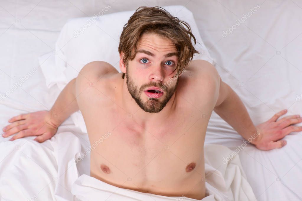 A young man waking up in bed and stretching his arms. Handsome man using clock in bed after waking up in the morning. Happy men in bed.