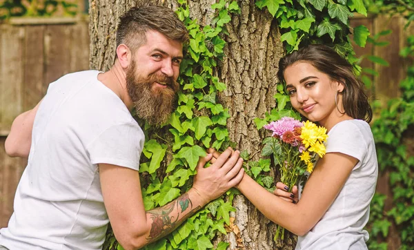 Pareja enamorada cita romántica paseo naturaleza árbol fondo. Fecha agradable en el entorno de la naturaleza. Hombre barbudo hipster sostiene la mano novia. Pareja enamorada apoyada en el maletero con hiedra. Unidos con la naturaleza — Foto de Stock