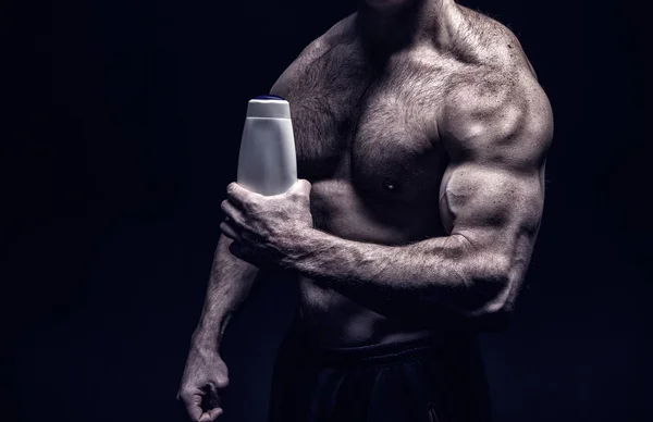 Knappe bodybuilder man met gespierd lichaam houdt shampoo fles — Stockfoto