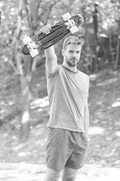 Που θέλουν να μάθουν ακραίο κόλπο. Ο τύπος κουβαλάει σανίδα της δεκάρας έτοιμη για βόλτα. Ο άνθρωπος σοβαρό πρόσωπο φέρει δεκάρα διοικητικό συμβούλιο πάρκο φύση φόντο defocused. Ο άνθρωπος θέλει να οδηγούν skateboard και σπορ τρόπο ζωής — Φωτογραφία Αρχείου