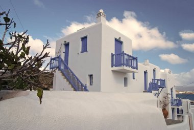 Mykonos, Yunanistan evlerde. Mavi boyalı pencere ve kapılarda güneşli gökyüzü badanalı binalarla. Tipik mimari ve tasarım. Bir Akdeniz Adası yaz tatili. Seyahat ve yolculuk kavramı