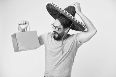 Adam neşeli yüzü fötr şapka alışveriş çantası sarı arka plan tutar. Sombrero içinde şenlikli sakallı adam. Adam şenlikli duygudurum alışveriş çantası tutar. Mevsimlik satış ve indirim. Tatil ve Hediyelik konsepti