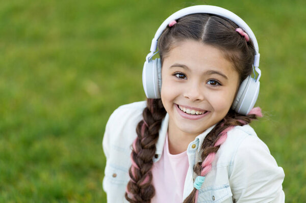 Fashion pretty cool girl in headphones listening music. Listen music while relaxing outdoor. Kid girl enjoy music while sit on green grass meadow. Pleasant leisure time. Child headphones listen music