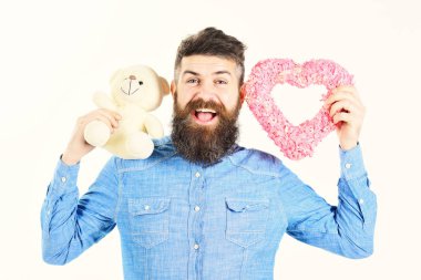 Sakallı adam aşk sembolleri tutar. Hippi kalp, oyuncak ayı ve mutlu neşeli yüz. Maço ile sakal gülümsüyor. Tebrik, dating, kutlama, flört kavramı. Sakallı adam komik hediyeler tutar