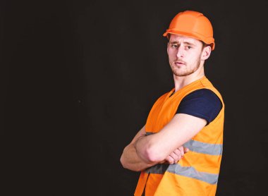 Güçlü Oluşturucusu kavramı. Kask, kask içinde adam tutun kollar göğüs üzerinde siyah arka plan geçti. İşçi, yüklenici, Oluşturucu üzerinde kas pazı ile ciddi bir yüz. Builder posing, kopya alanı kask içinde