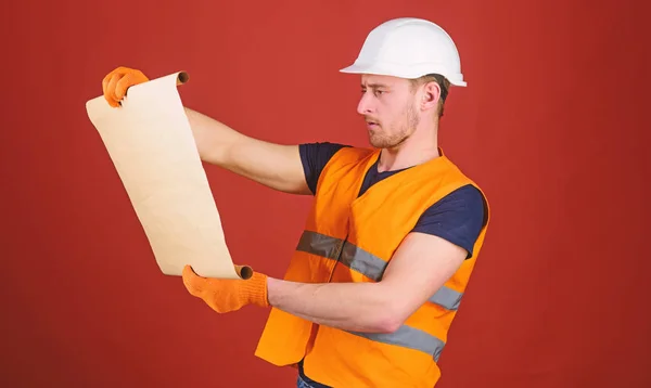 Engineering concept. Engineer, architect, labourer, builder on strict face holds old blueprint in hands. Man, handyman in helmet, hard hat holds building plan, red background — Stock Photo, Image