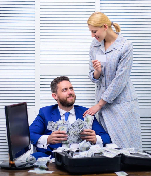 Business, people and finances concept. Case of money. Happy and excited man sitting at table covered with money and rejoices with girl secretary. Black cash.
