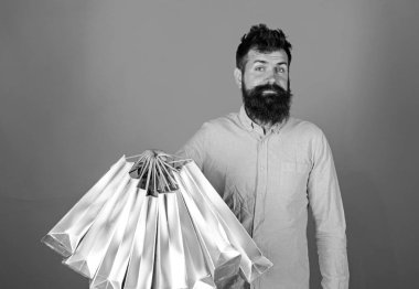 Gülümseyen yüzü üzerinde hipster bağımlısı alışveriş veya Alışverişkoliğin. Satış sezon indirimlerle alışveriş adam. Adam sakal ve bıyık tutan grup alışveriş torbaları, kırmızı arka plan ile. Alışveriş kavramı