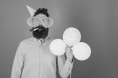 Kutlama kavramı. Hippi dev güneş gözlüğü Doğum günü kutluyor. Sakal ve bıyık sakin yüz darbeler içine parti boynuz, mavi arka plan üzerinde olan adam. Hava balonları ile parti şapkalı adamı kutluyor