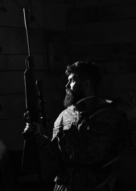 Avcı kavramı. Avcı silahı ve karanlıkta ışıklı geyik boynuzları ile acımasız. Sakallı kamuflaj elbiseler, koyu arka plan giyer. Maço gamekeepers evinde avlamaya hazır sıkı yüzünde