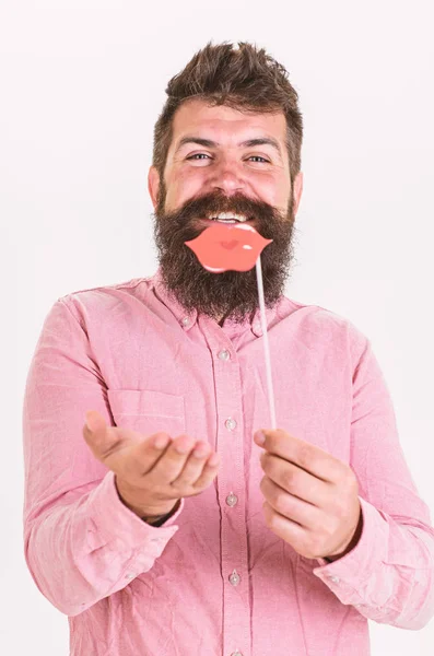 Hipster with beard and mustache on cheerful face posing with photo booth props, copy space. Man holding party props lips, white background. Guy sending air kiss with red lips. Photo booth fun concept — Stock Photo, Image