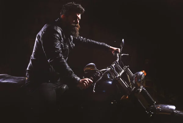 Homem com barba, motociclista de jaqueta de couro sentado em moto no escuro, fundo preto. Conceito de piloto nocturno. Macho, motociclista brutal em couro jaqueta equitação motocicleta à noite, espaço cópia — Fotografia de Stock