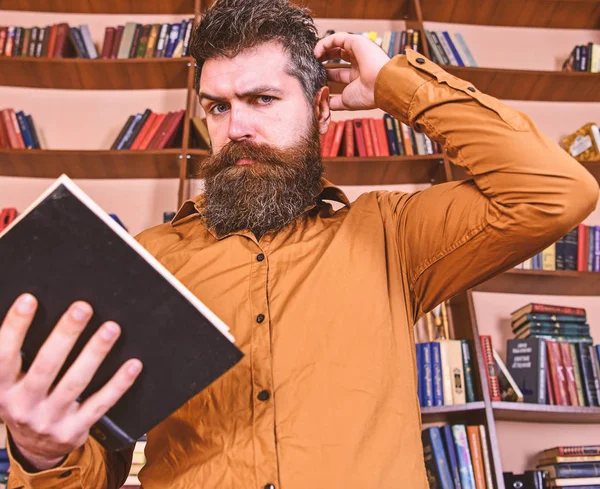 Portrait d'homme avec barbe et de bons yeux lisant livre à la main sur fond de bibliothèque. Éducation et science concept. Scientifique occupé à lire le livre. Professeur, étudiant barbu étudiant à la bibliothèque — Photo