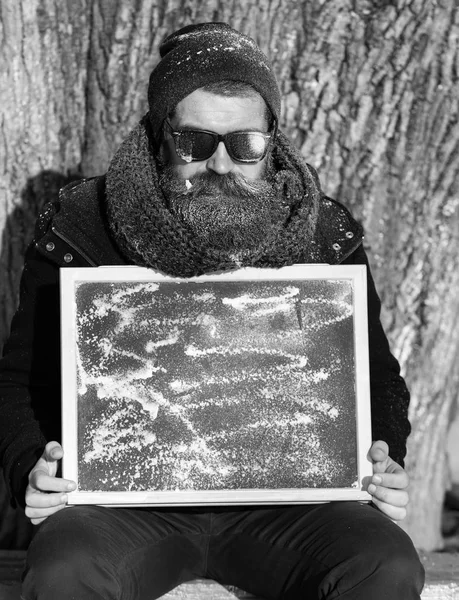 Hombre, hipster, con barba y bigote en gafas de sol negras cubiertas de escarcha blanca da doble gesto ok con tablero negro en el día de invierno sobre fondo natural, copia spac —  Fotos de Stock