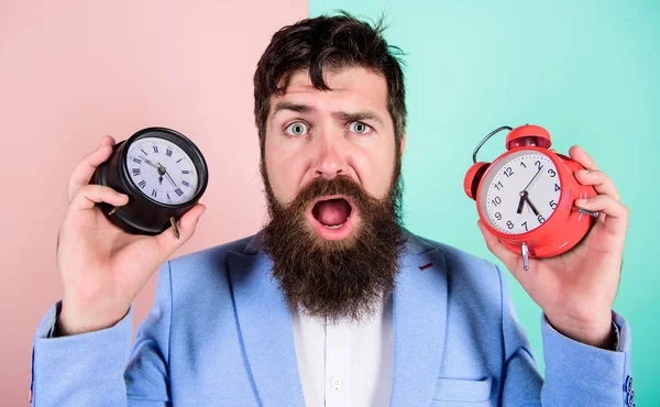 Cambia el reloj y arruina tu salud. El hombre barbudo hipster sostiene dos relojes diferentes. Tipo sin afeitar desconcertado cara tener problemas con el cambio de tiempo. Los cambios en las zonas horarias afectan la salud. Zona horaria —  Fotos de Stock