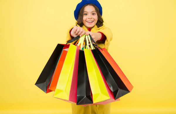 Fashionista adore shopping. Obsessed with shopping. Girl cute kid hold shopping bags on yellow background. Mid season sale. Shop with discount card. Get discount shopping on birthday or holiday