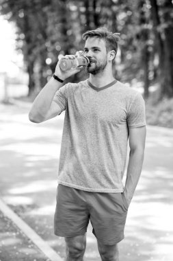 Uzun antrenman bitti. Atletik görünüşlü bir adam şişeyi suyla tutar. Sporcu güneşli bir günde parkta antrenmandan sonra su içer. Sportif giysiler içindeki erkek sporcu ferahlatıcı maden suyu içer.
