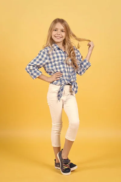 Маленька дівчинка посміхається в сорочці і штанях на помаранчевому фоні — стокове фото