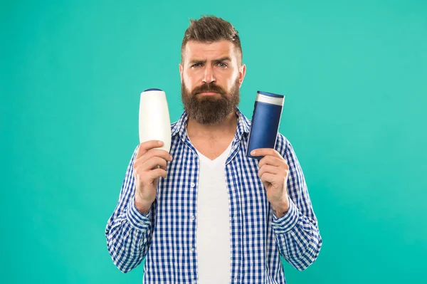 Make right choice. Man bearded hipster choose shampoo or shower gel. Hair care and skin treatment. Choose beauty product. Barbershop and hair care. Wash hair with shampoo. Hair conditioner or lotion