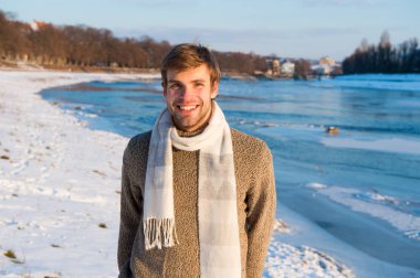 Erkek triko kazak yün, ipek eşarp standında nehir arka plan donmuş tıraşsız yakışıklı hippi. Kış manzara güzellik. Adam kış güneşli gün tadını çıkarın. Kış giysileri ısınma ördü. Kış modası