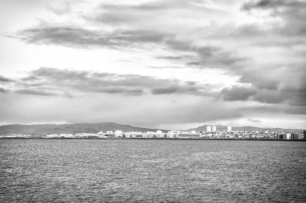 Città sulla costa del mare Islanda. Concetto di paesaggio marino scandinavo. Calma superficie dell'acqua e città con edifici alti architettura moderna. Città scandinava in riva al mare. Reykjavik paesaggio marino drammatico cielo nuvoloso — Foto Stock