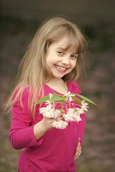 Pequena menina com rosto sorridente segurando flor sakura rosa — Fotografia de Stock