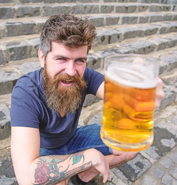 Hipster na wesołą twarz pije piwo odkryty. Koncepcja uroczystości. Człowiek z broda i wąsy posiada szkło z piwem, podczas gdy siedzi na kamienne schody, rozmyte. Facet, podnoszenie się szkło z piwo — Zdjęcie stockowe