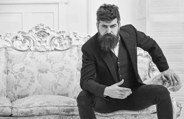 Concepto de moda y estilo. Hombre con barba y bigote con traje clásico, elegante atuendo de moda. Macho atractivo y elegante en serio, cara reflexiva sentado en el sofá de lujo a la antigua —  Fotos de Stock