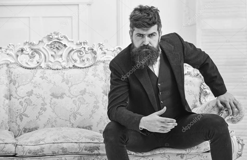 Fashion and style concept. Man with beard and mustache wearing classic suit, stylish fashionable outfit. Macho attractive and elegant on serious, thoughtful face sitting on old fashioned luxury sofa