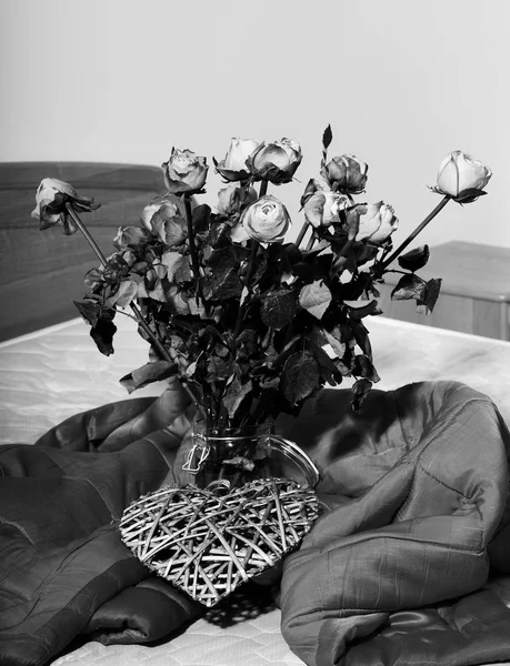 Bouquet di rose arancioni in vaso trasparente con decorativo cuore grigio valentino poggia sul letto sotto coperta rossa su fondo parete rosa — Foto Stock