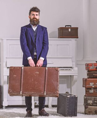 Bagaj ve seyahat kavramı. Maço sıkı yüzünde şık duruyor ve büyük vintage çanta taşır. Adam, Gezgin sakallı ve bıyıklı Bagaj, lüks beyaz iç arka plan