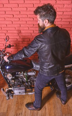 Sakallı, motorcu motorlu bisiklet garaj, tuğla duvar arka plan yakınındaki deri ceketli adam. Erkeksi hobi kavramı. Yenilikçi, vahşi Motorcu deri ceketli motosiklet üzerinde arka görüş oturur