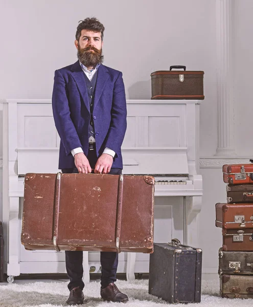 Baggage and travelling concept. Macho stylish on strict face stands and carries big vintage suitcase. Man, traveller with beard and mustache with baggage, luxury white interior background